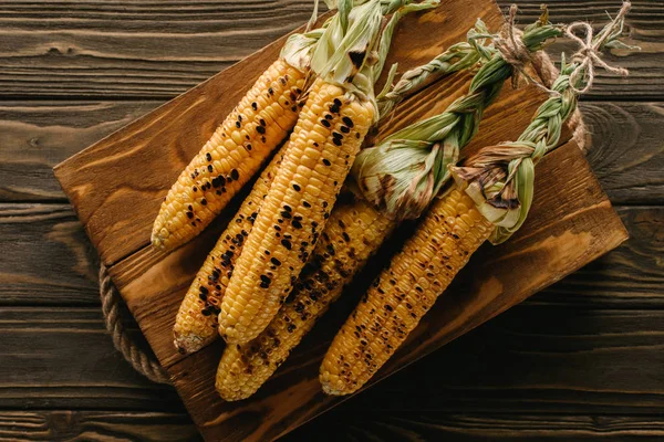 Elevated view of delicious grilled corn on cutting board on wooden table — Stock Photo