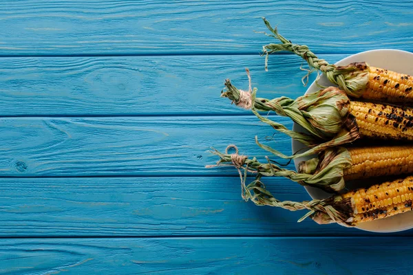 Vista superior de maíz a la parrilla en placa sobre mesa de madera azul - foto de stock