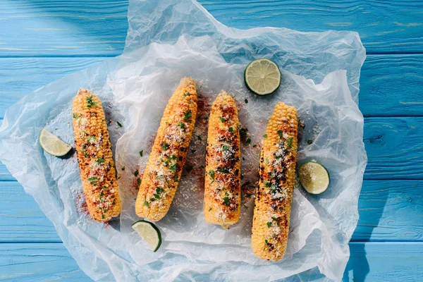 Ansicht von gegrilltem gesalzenem Mais mit Limettenscheiben auf Backpapier auf Holztisch — Stockfoto