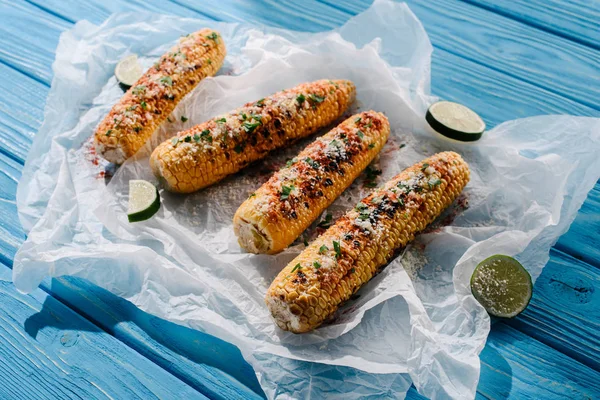 Selective focus of grilled salted corn with lime slices on baking paper on wooden table with sunlight — Stock Photo