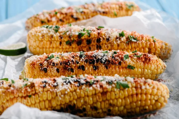 Close up view of grilled salted corn with lime slices on baking paper — Stock Photo