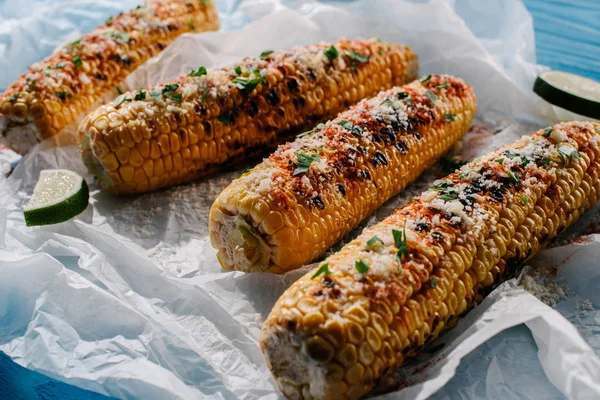 Selective focus of grilled salted corn with lime slices on baking paper on wooden table — Stock Photo