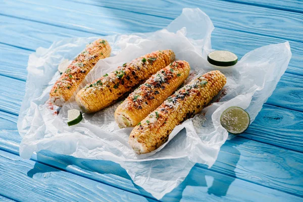 Close up view of grilled salted corn with lime slices on baking paper on wooden table with sunlight — Stock Photo