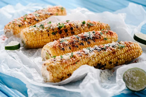 Close up view of grilled corn with lime slices on baking paper on wooden table — Stock Photo