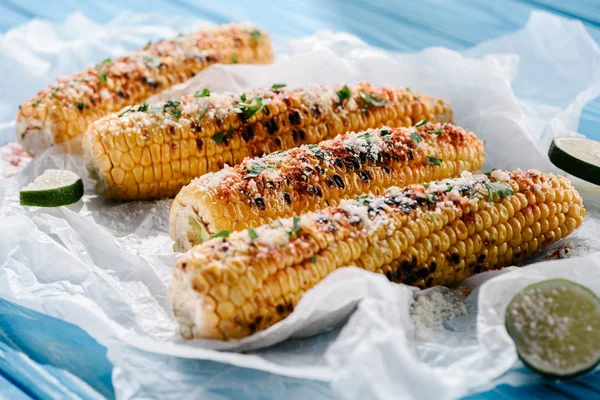 Vue rapprochée du maïs grillé avec des tranches de lime sur du papier cuisson sur une table en bois — Photo de stock