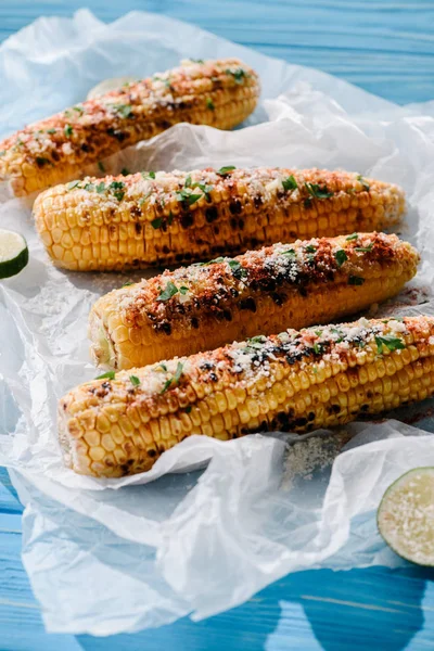 Close up view of delicious grilled corn with lime slices on baking paper on wooden table — Stock Photo