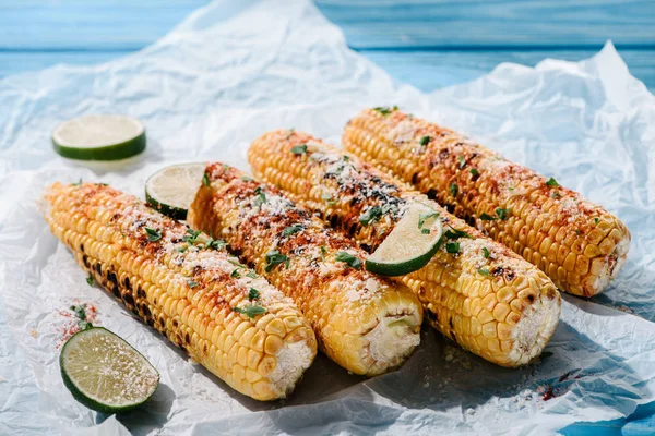 Vue rapprochée de délicieux maïs grillé salé avec des tranches de lime sur du papier cuisson — Photo de stock