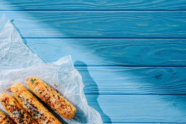 Vue du dessus du papier cuisson avec maïs grillé sur table en bois avec lumière du soleil — Photo de stock