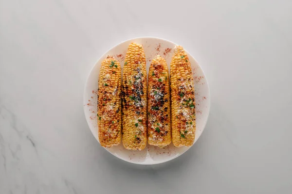 Vista superior de maíz a la parrilla con sal y especias de chile en el plato en la mesa de mármol - foto de stock
