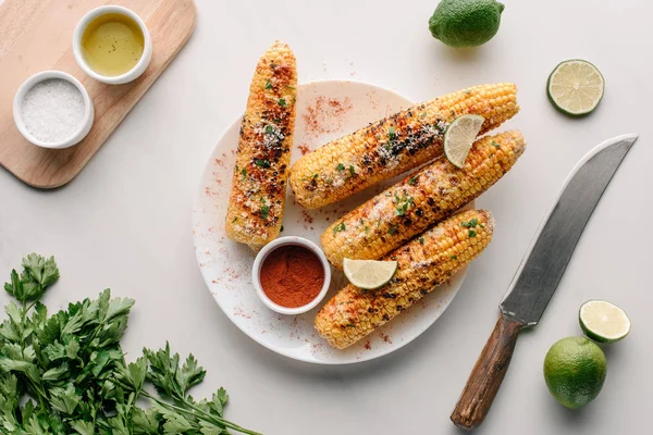 Vue du dessus du maïs salé grillé avec tranches de citron vert et piment sur la table — Photo de stock