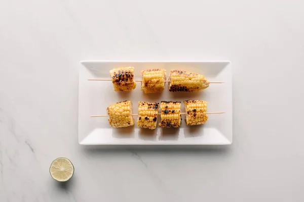 Top view of grilled corn on plate near lime slice on marble table — Stock Photo