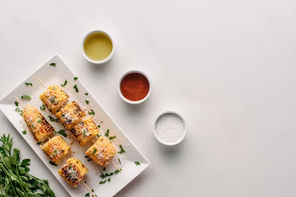 Vue du dessus du persil, maïs grillé sur plaque avec sel, huile et piment sur table en marbre — Photo de stock