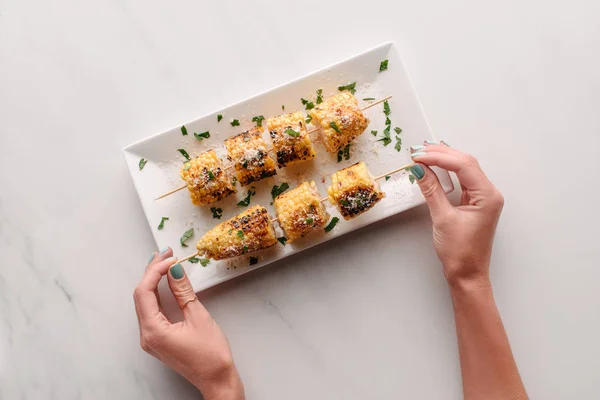 Cropped image of woman taking grilled corn from plate on marble table — Stock Photo