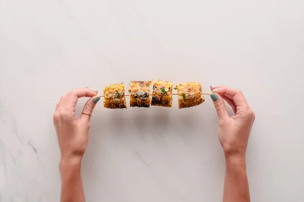 Cropped image of woman holding delicious grilled corn over marble table — Stock Photo