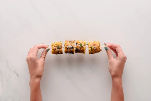 Imagen recortada de la mujer sosteniendo delicioso maíz a la parrilla sobre la mesa de mármol - foto de stock