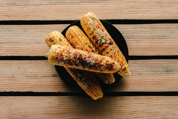 Vista superior de delicioso maíz salado a la parrilla en el plato en la mesa de madera - foto de stock