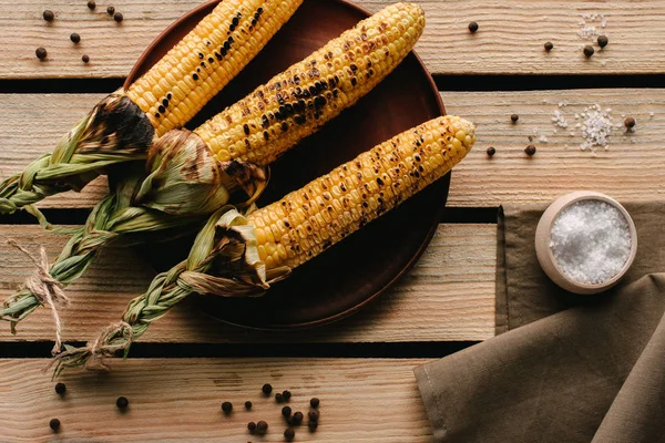 Вид зверху на смажену кукурудзу на тарілці і сіль на дерев'яному столі з кухонним рушником — стокове фото