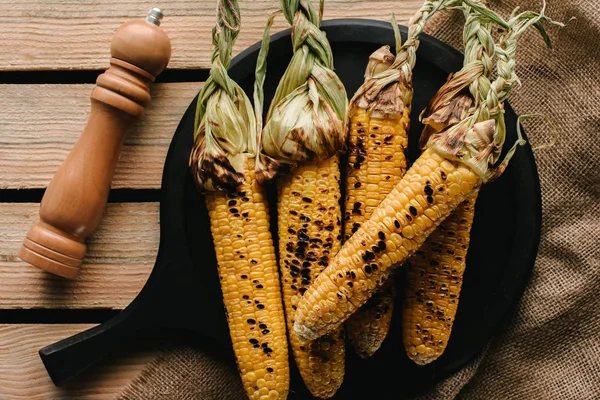 Top view of grilled corn, salt grinder on wooden table with sackcloth — Stock Photo