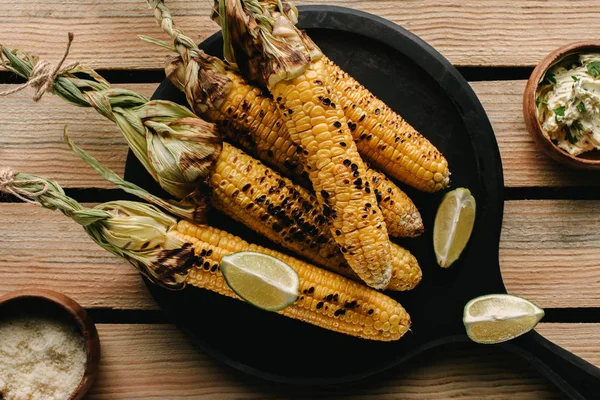 Top view of grilled corn, lime slices and butter with parsley on wooden table — Stock Photo