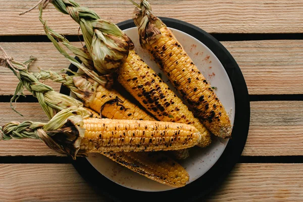 Vista superior del delicioso maíz a la parrilla en el plato en la mesa de madera - foto de stock