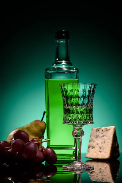 Close-up shot of absinthe with fruits and cheese on mirror surface on dark blue background — Stock Photo