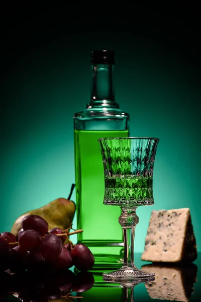 Primer plano de absenta con frutas y queso en la superficie del espejo sobre fondo azul oscuro - foto de stock