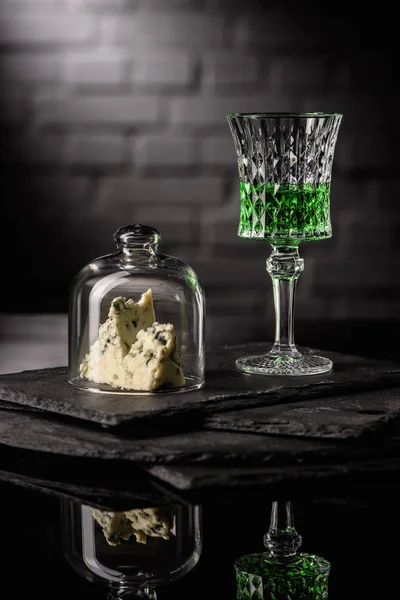 Close-up shot of glass of absinthe with slice of cheese on dark brick wall background — Stock Photo