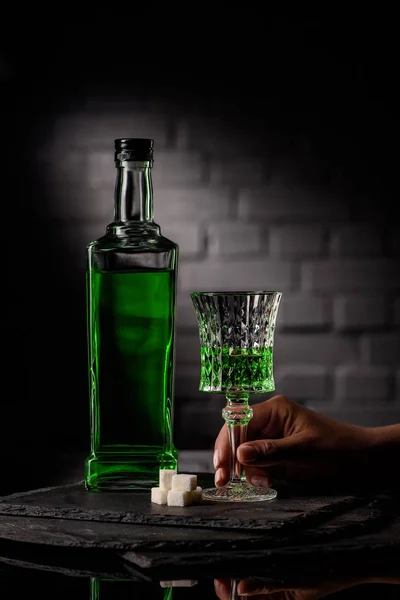 Cropped shot of woman holding glass of absinthe on dark brick wall background — Stock Photo