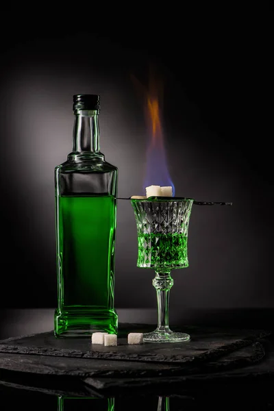 Gros plan de la cuillère avec des cubes de sucre sur la combustion de l'absinthe dans le verre sur fond sombre — Photo de stock