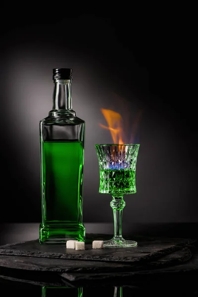 Gros plan de bouteille et verre d'absinthe brûlante sur fond sombre — Photo de stock