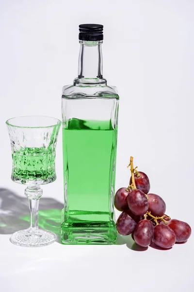 Vidro de cristal e garrafa de absinto com ramo de uvas em branco — Fotografia de Stock