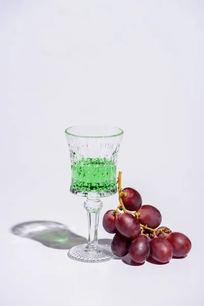 Crystal glass of absinthe with branch of grapes on white — Stock Photo