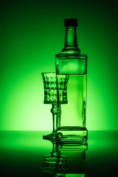 Bottle of absinthe with lead glass on mirror surface and dark green background — Stock Photo