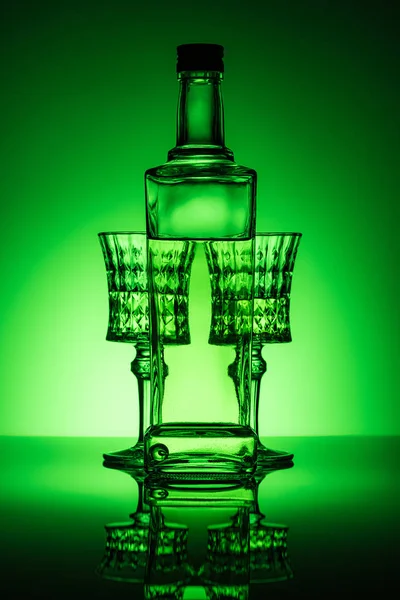 Flasche Absinth mit Kristallgläsern auf Spiegeloberfläche und dunkelgrünem Hintergrund — Stockfoto