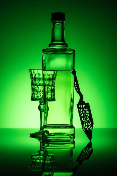 Botella de absenta con cristal y cuchara sobre superficie reflectante y fondo verde oscuro - foto de stock