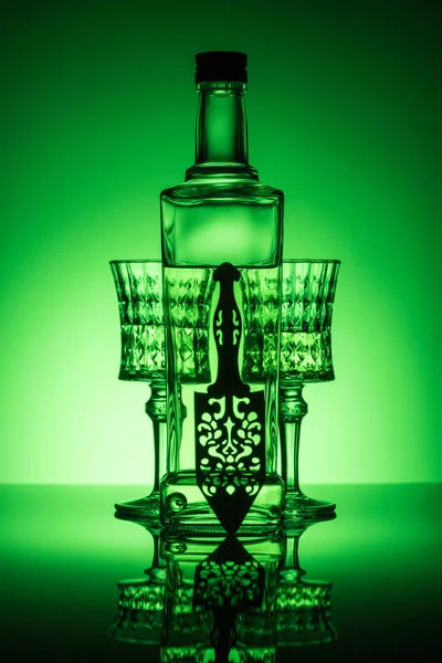 Бутылка абсента с хрустальными стеклами на отражающей поверхности и темно-зеленым фоном — стоковое фото