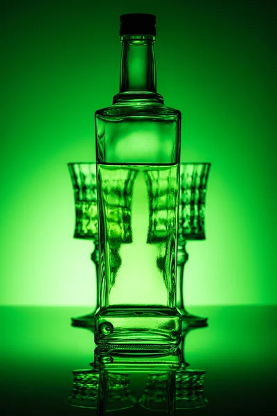 Bouteille d'absinthe avec des lunettes sur la surface du miroir et fond vert foncé — Photo de stock