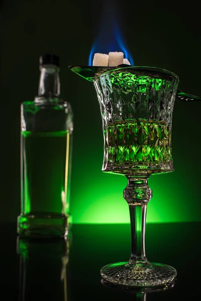 Verre et bouteille d'absinthe avec sucre brûlant sur cuillère sur surface réfléchissante et fond vert foncé — Photo de stock