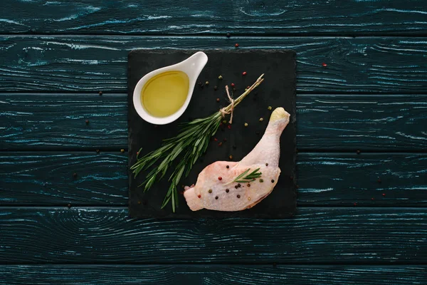 Vue du dessus de la cuisse de poulet avec romarin, grains de poivre et huile sur pierre ardoise noire — Photo de stock