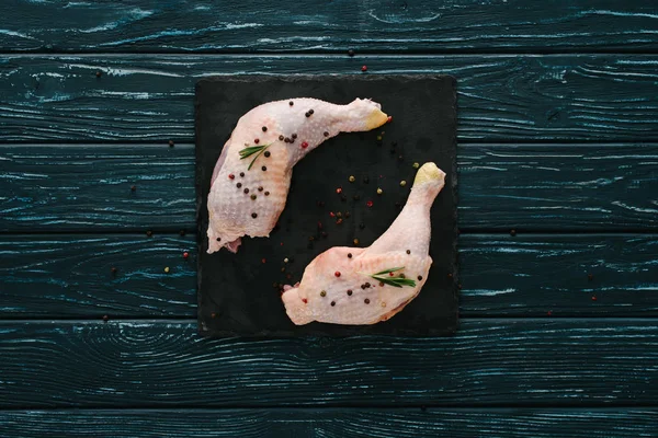 Top view of chicken legs with pepper corns on black slate — Stock Photo