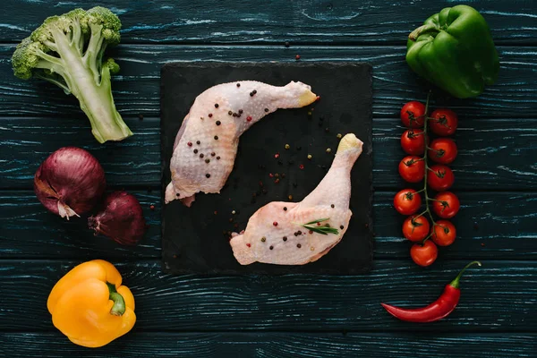 Vista superior de patas de pollo en pizarra de piedra con diferentes verduras en la mesa de madera verde oscuro - foto de stock