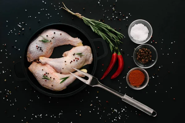 Acostado plano con patas de pollo en la sartén con especias y tenedor de carne en la mesa negra - foto de stock