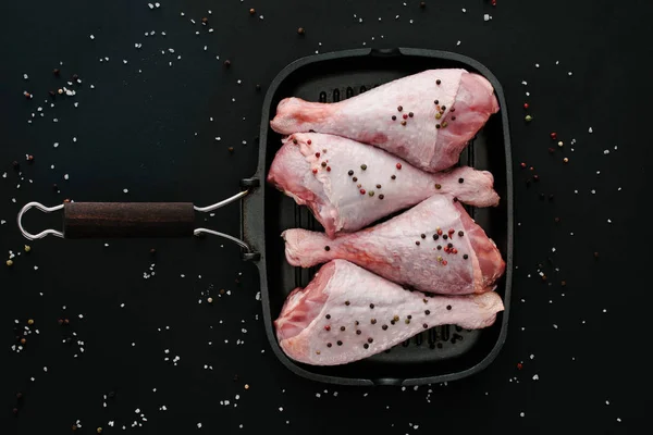 Vue du dessus des cuisses de poulet avec des grains de poivre et du sel dans une poêle sur fond noir — Photo de stock
