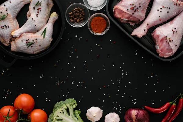 Flat lay with chicken and turkey legs in pans with vegetables and spices on dark tabletop — Stock Photo