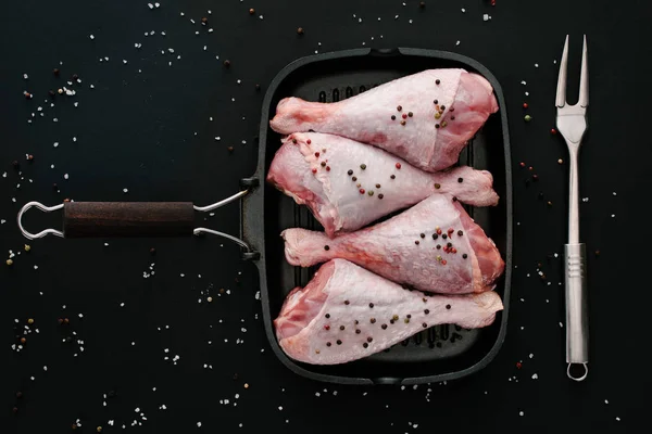 Deitado plano com pernas de peru cru com grãos de pimenta e sal na panela de grelha com garfo de carne em preto — Fotografia de Stock