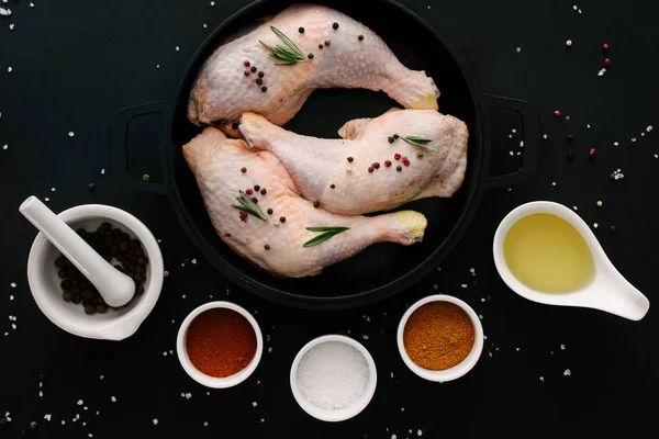 Плоская лежа с куриными ножками на сковороде со специями и маслом на черном столе — стоковое фото