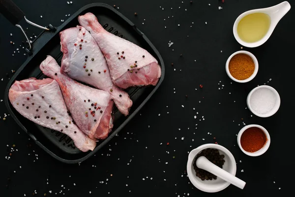 Flat lay with turkey legs on grill pan with pepper corns, salt, oil and spices on black table — Stock Photo