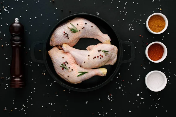 Flat lay with chicken legs on pan with pepper corns and paprika on black table — Stock Photo