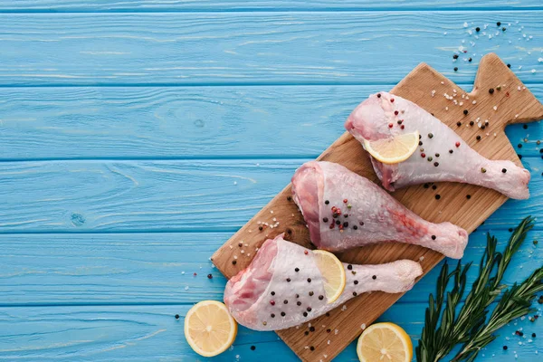 Vista superior de patas de pollo crudas con granos de pimienta, limón y romero sobre tabla de madera - foto de stock