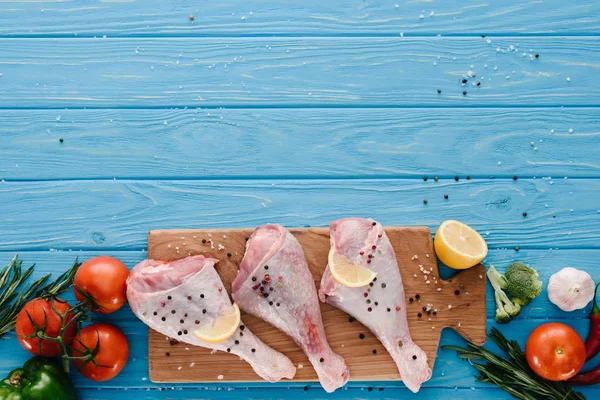 Acostado plano con patas de pavo sobre tabla de madera con diferentes verduras en la mesa azul - foto de stock